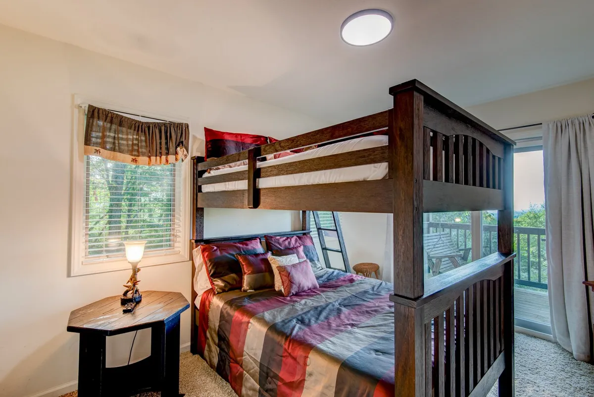 A warm and inviting bunk room with a bunk bed, decorative pillows, a bedside table, and a window with curtains letting in soft light. The space is both playful and practical, designed for children or families sharing stories late into the night.