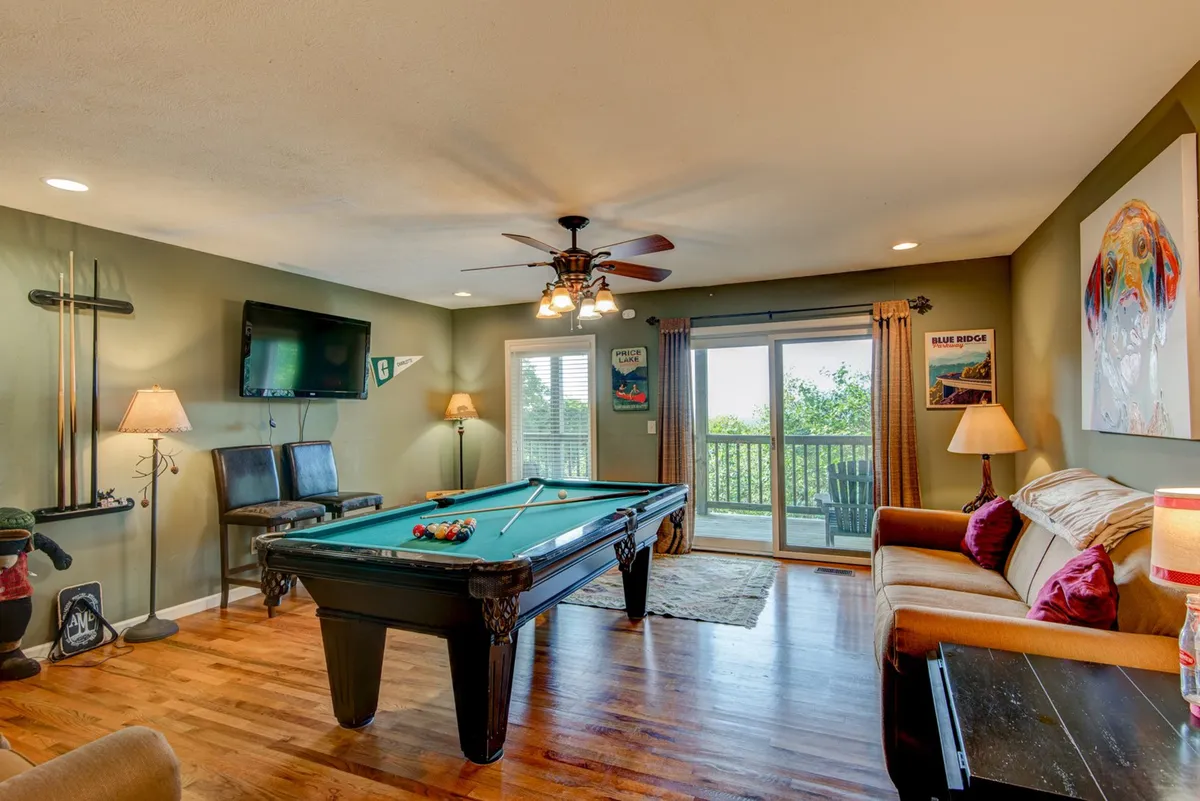 A vibrant recreation area featuring a pool table, a comfortable sofa, large windows bringing in natural light, and decorative art on the walls. The setup is lively, ideal for group activities, and hints at a fun, social atmosphere.