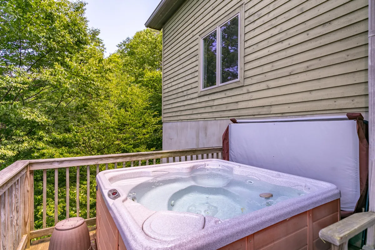 A serene wooden deck features a bubbling hot tub, surrounded by trees and greenery. The inviting space suggests a relaxing post-adventure retreat where both guests and their pets can unwind after a day outdoors.