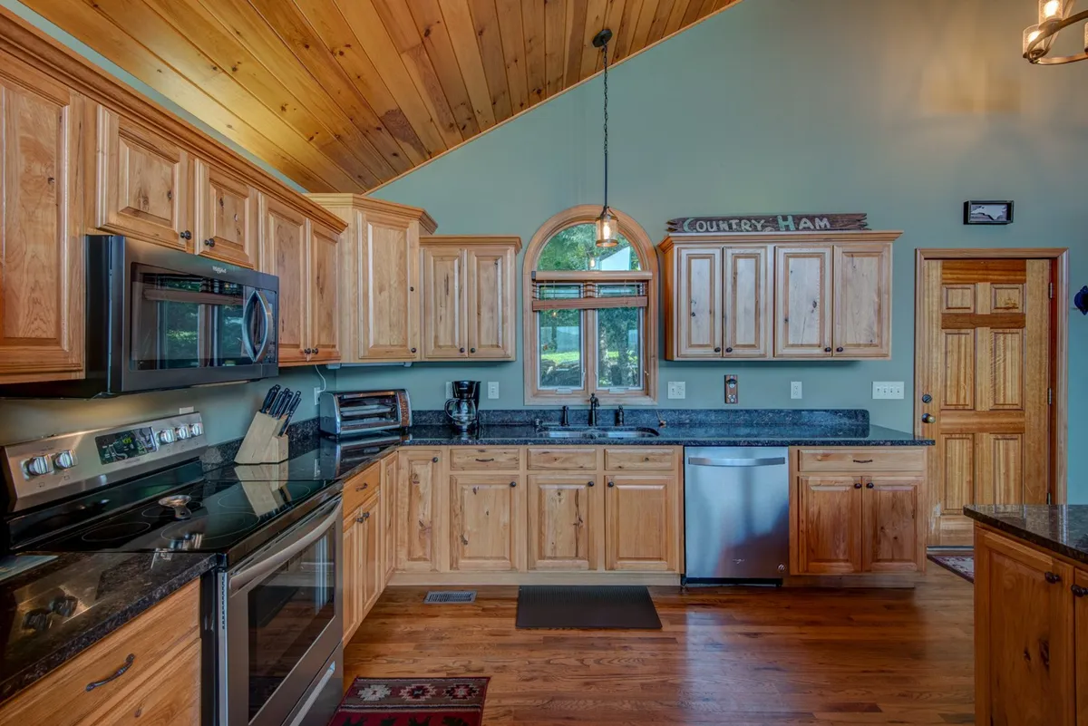 A modern kitchen with black granite countertops, wooden cabinetry, stainless steel appliances, and a large window flooding the space with natural light. The kitchen feels both functional and luxurious.