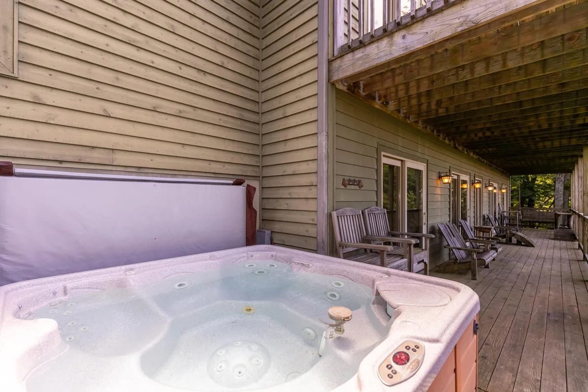 This exterior image features a hot tub on a wooden deck with comfortable seating and sturdy wooden beams, all set against a backdrop of mountain views and greenery. The space invites relaxation after a day of outdoor activities.