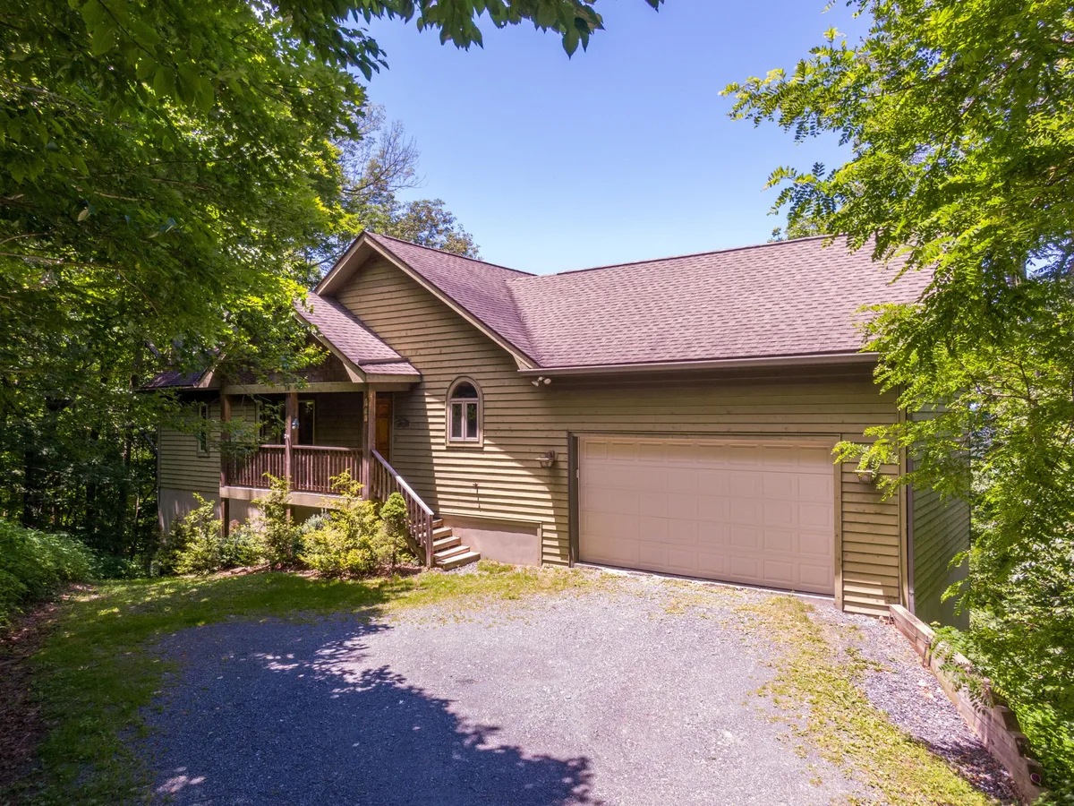 The front porch and natural landscaping of the house are shown, including a clear view of the attached garage. The inviting porch offers a space for relaxation, while the garage provides convenient, winter-ready access.
