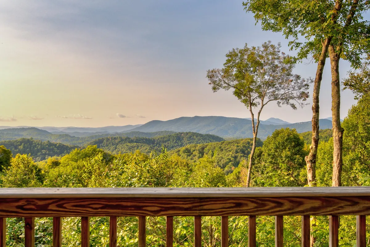 This image showcases a stunning mountain range framed by lush greenery and a wooden deck railing. The tranquil atmosphere and panoramic view create an inviting space for guests to relax and soak in the natural beauty of the High Country.