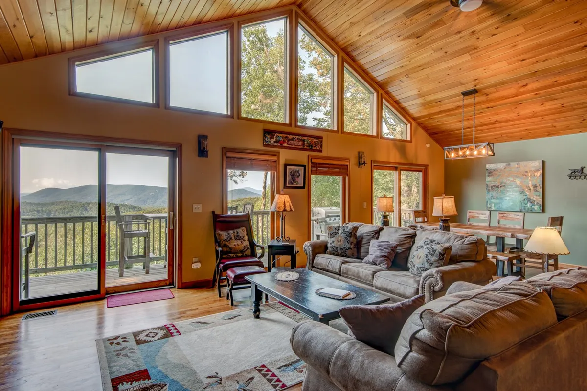 A bright, open-plan great room with large windows framing mountain views, comfortable sofas, and a central coffee table. The inviting space is ideal for family gatherings, game nights, and enjoying the scenic landscape from indoors.