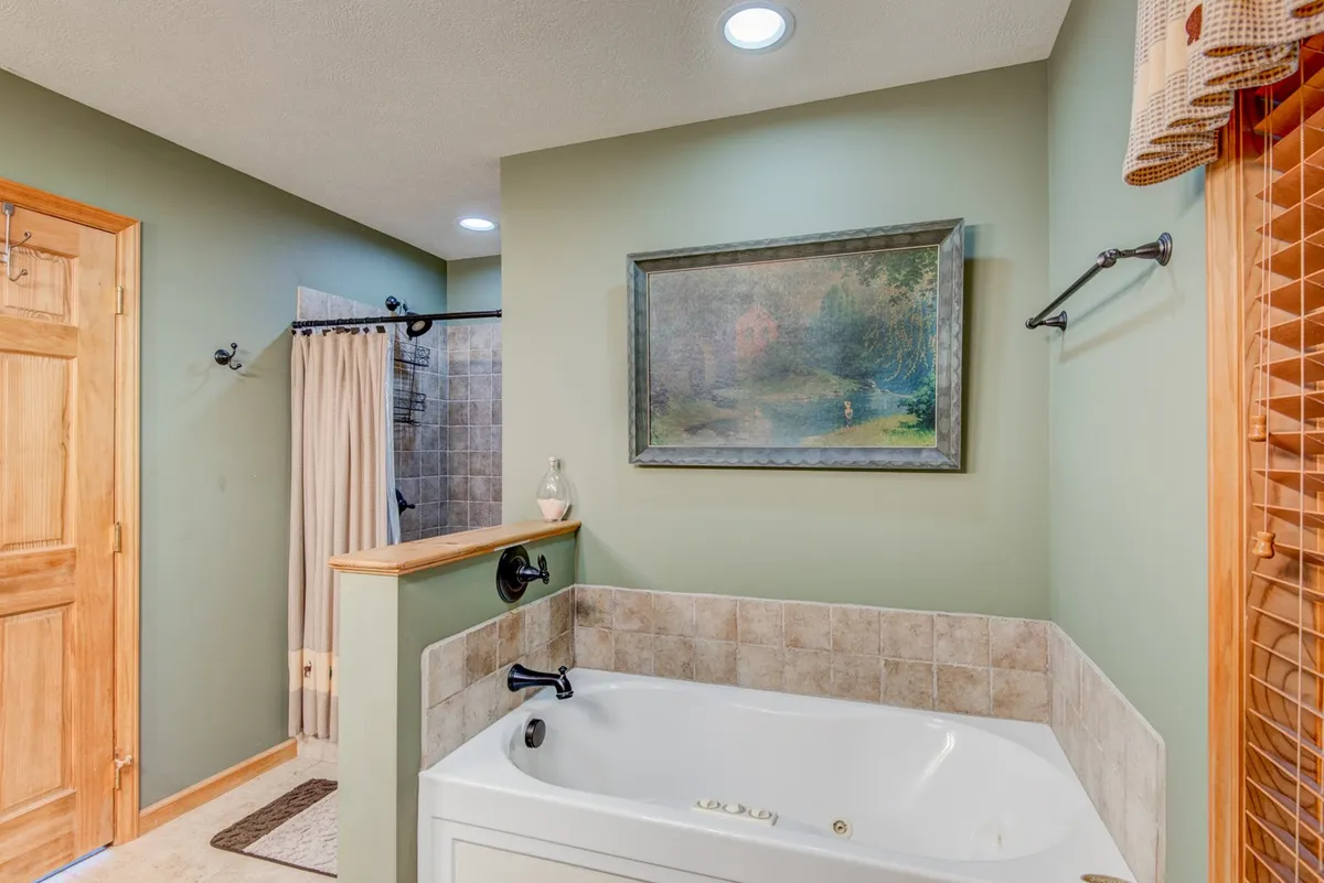 A serene bathroom with a jacuzzi tub positioned beneath a framed painting and adjacent to a wooden door. The setup emphasizes relaxation and offers a peaceful retreat for a soothing soak after a long day.