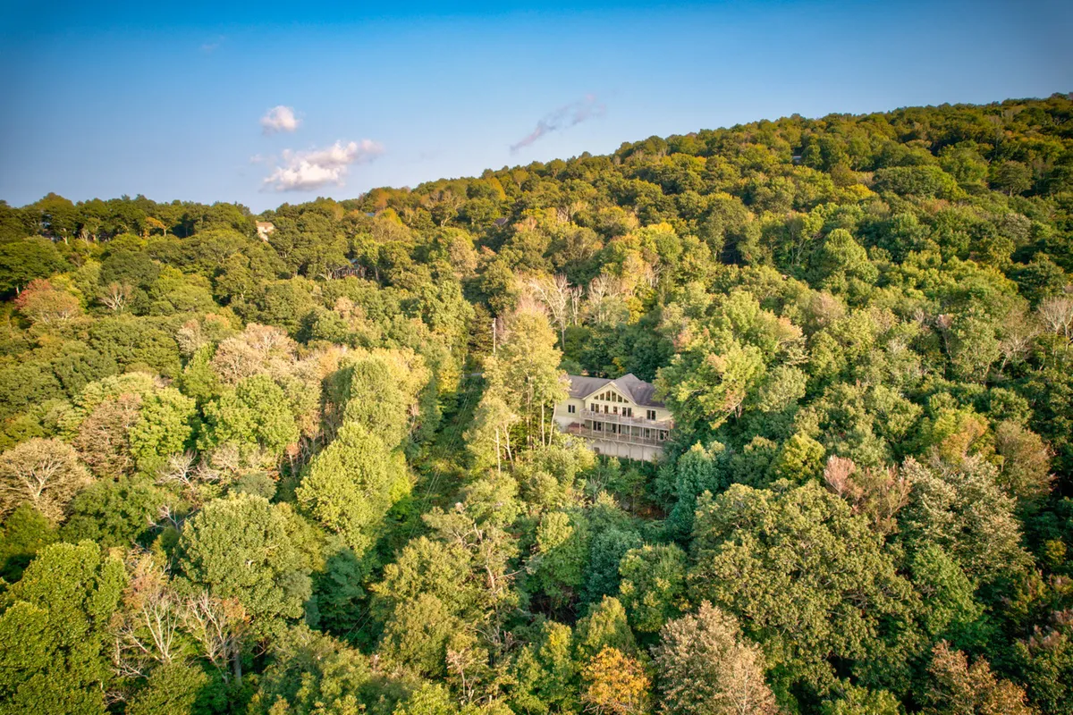 A welcoming exterior view of the house nestled among tall trees, with an open sky above and wraparound porch visible. The setting exudes tranquility and offers hints of the natural surroundings guests will enjoy.